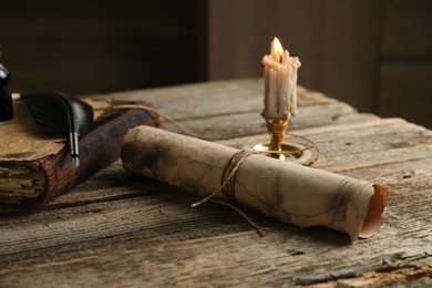Photo of Old paper scroll, book, feather and burning candle on wooden table, closeup