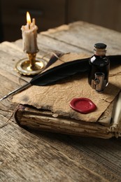 Photo of Old paper scroll, book, feather, inkwell and burning candle on wooden table, closeup