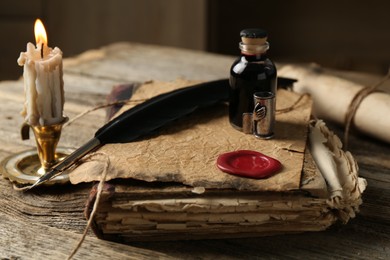 Photo of Old paper scroll, book, feather, inkwell and burning candle on wooden table, closeup