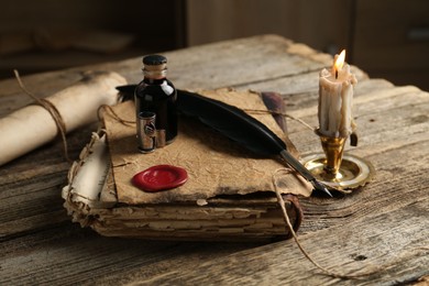 Photo of Old paper scroll, book, feather, inkwell and burning candle on wooden table, closeup