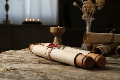 Photo of Old paper scrolls and burning candle on wooden table, closeup