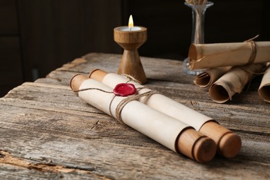 Photo of Old paper scrolls and burning candle on wooden table, closeup