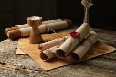 Photo of Old paper scrolls and burning candle on wooden table, closeup