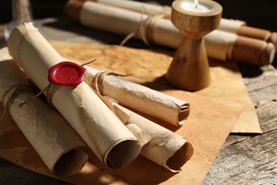 Photo of Old paper scrolls and burning candle on wooden table, closeup