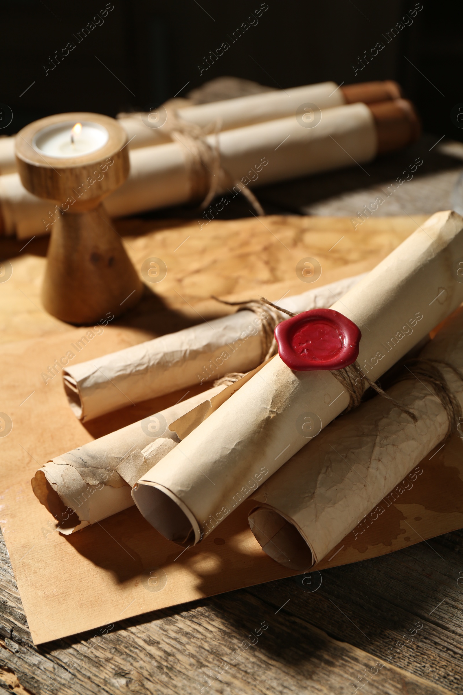 Old paper scrolls and burning candle on wooden table, closeup Photo of Old paper scrolls and burning candle on wooden table, closeup