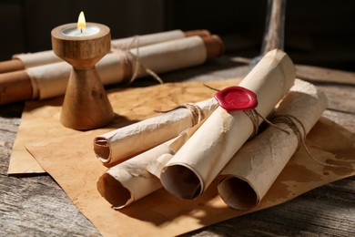 Photo of Old paper scrolls and burning candle on wooden table, closeup