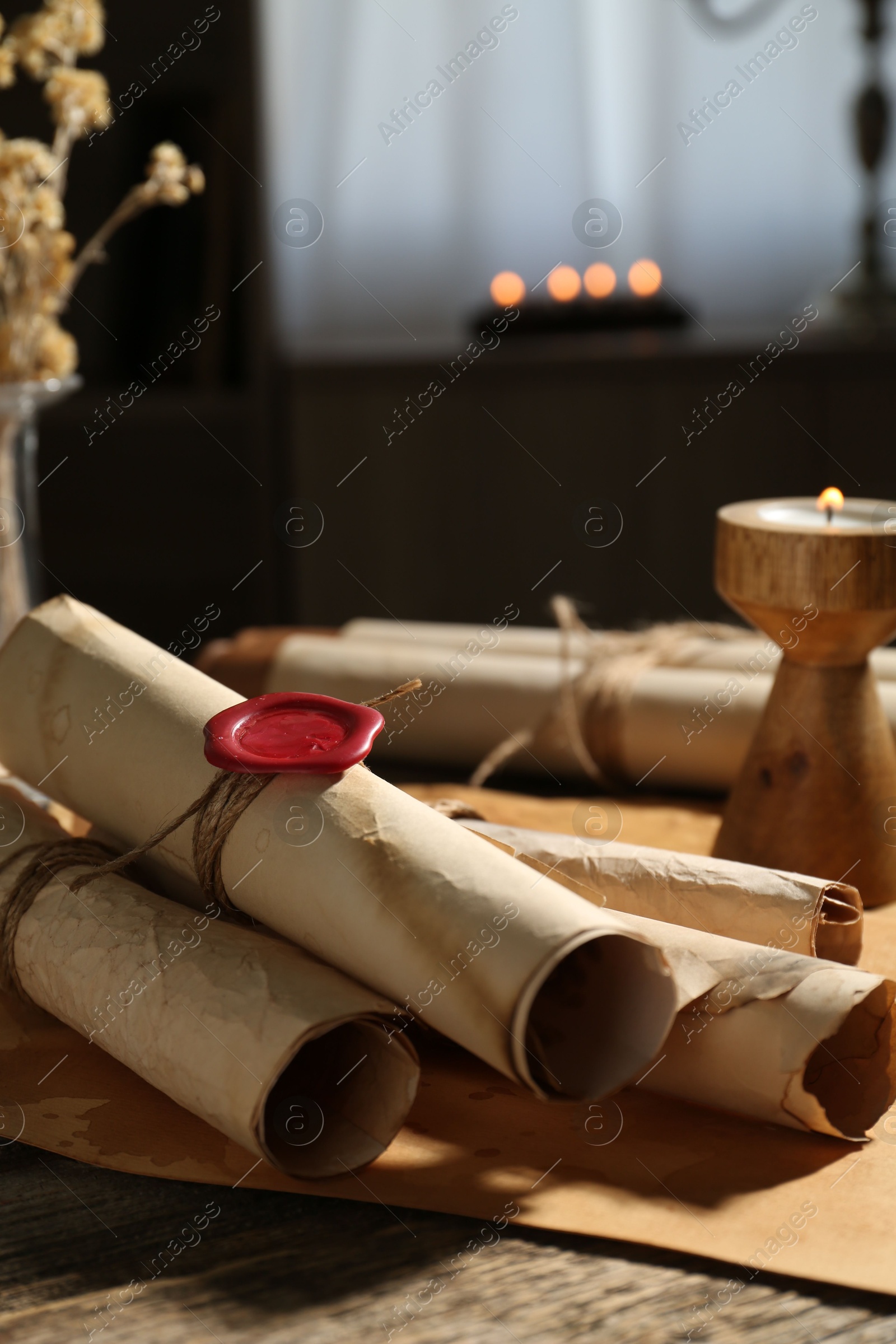 Old paper scrolls and burning candle on wooden table, closeup Photo of Old paper scrolls and burning candle on wooden table, closeup