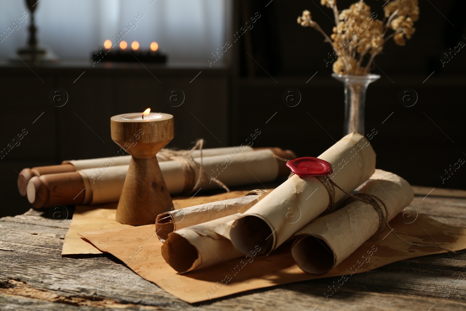 Old paper scrolls and burning candle on wooden table, closeup Photo of Old paper scrolls and burning candle on wooden table, closeup
