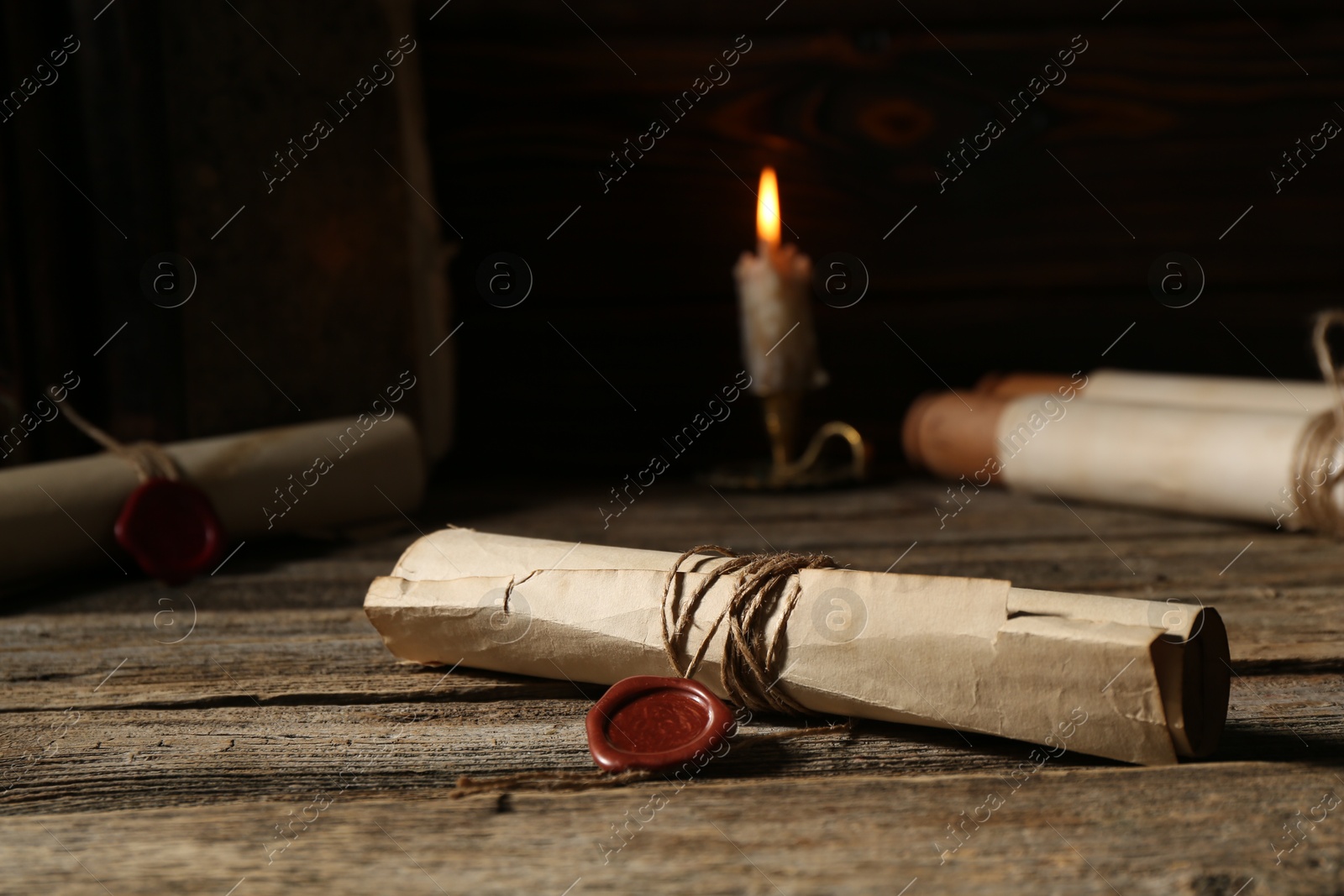 Old rolled paper scrolls and burning candle on wooden table, closeup Photo of Old rolled paper scrolls and burning candle on wooden table, closeup