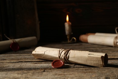 Photo of Old rolled paper scrolls and burning candle on wooden table, closeup