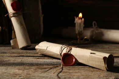 Photo of Old rolled paper scrolls and burning candle on wooden table, closeup
