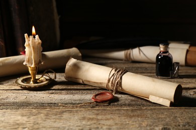 Photo of Old rolled paper scrolls and burning candle on wooden table, closeup
