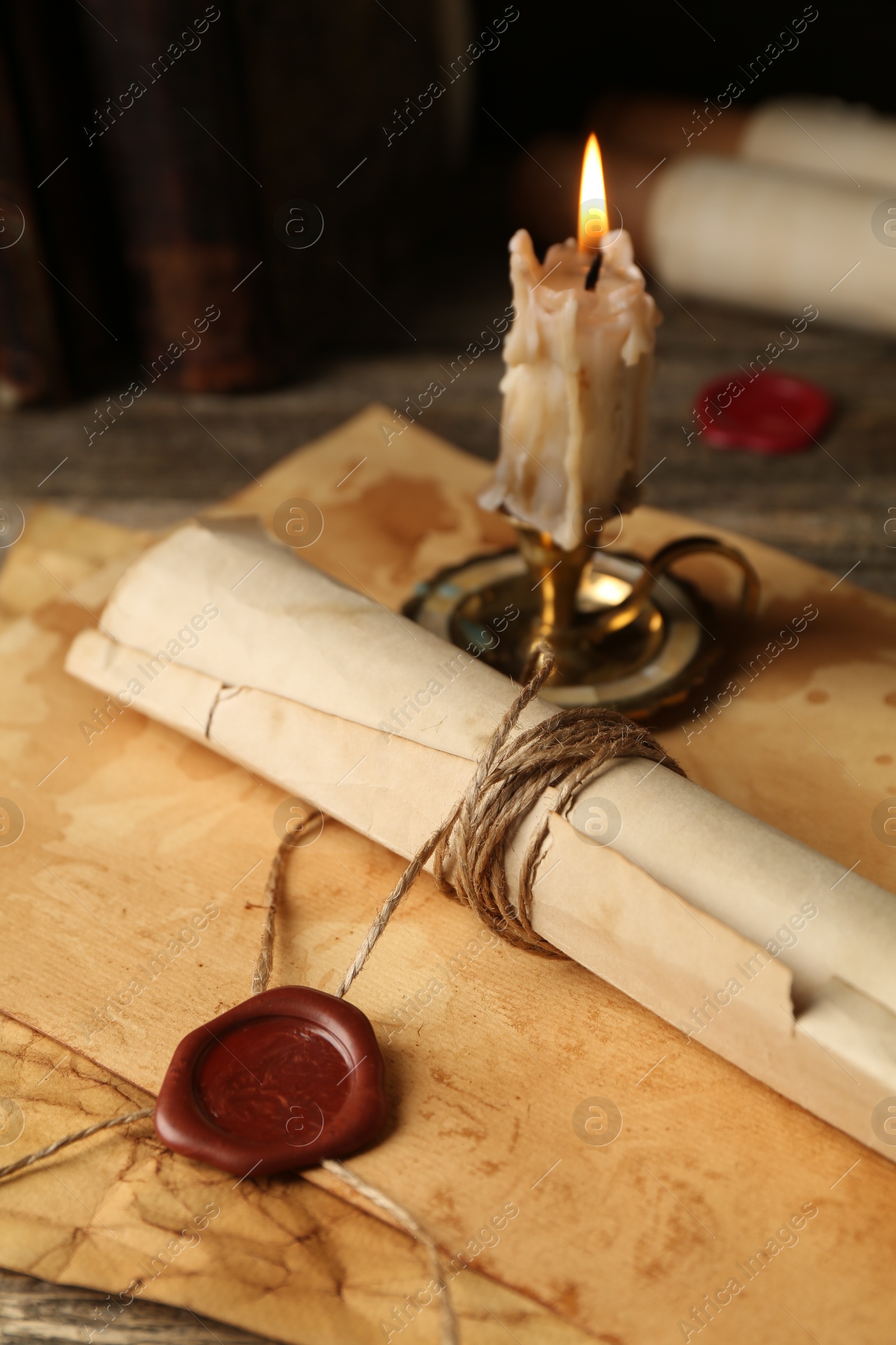 Photo of Old rolled paper scroll, sheets and burning candle on wooden table, closeup