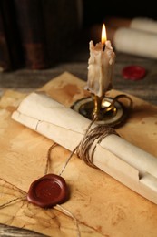 Photo of Old rolled paper scroll, sheets and burning candle on wooden table, closeup