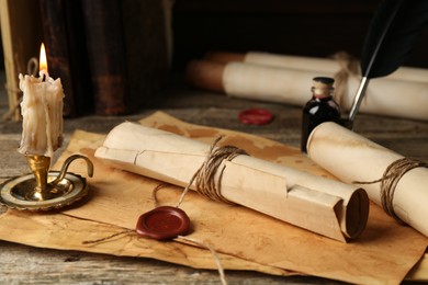 Photo of Old rolled paper scrolls, sheets and burning candle on wooden table, closeup