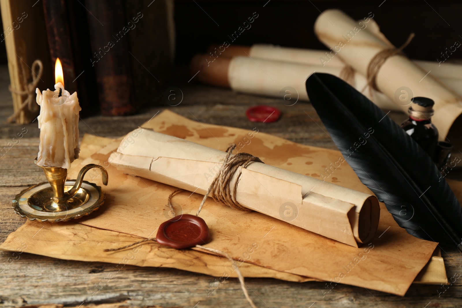 Old rolled paper scrolls, sheets and burning candle on wooden table, closeup Photo of Old rolled paper scrolls, sheets and burning candle on wooden table, closeup