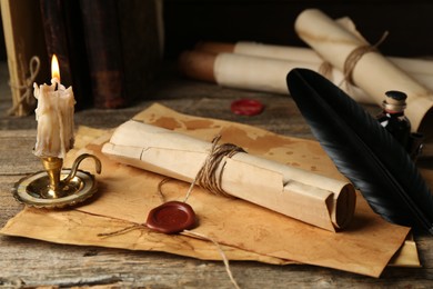 Photo of Old rolled paper scrolls, sheets and burning candle on wooden table, closeup