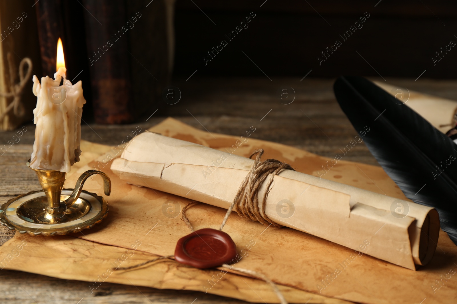 Photo of Old rolled paper scroll, sheets and burning candle on wooden table, closeup