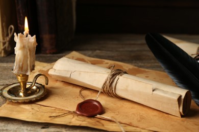 Photo of Old rolled paper scroll, sheets and burning candle on wooden table, closeup
