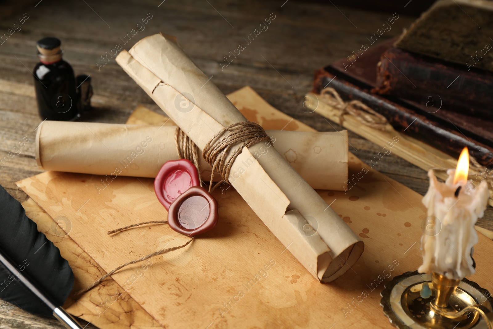 Old paper scrolls and burning candle on wooden table, closeup Photo of Old paper scrolls and burning candle on wooden table, closeup