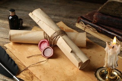 Photo of Old paper scrolls and burning candle on wooden table, closeup