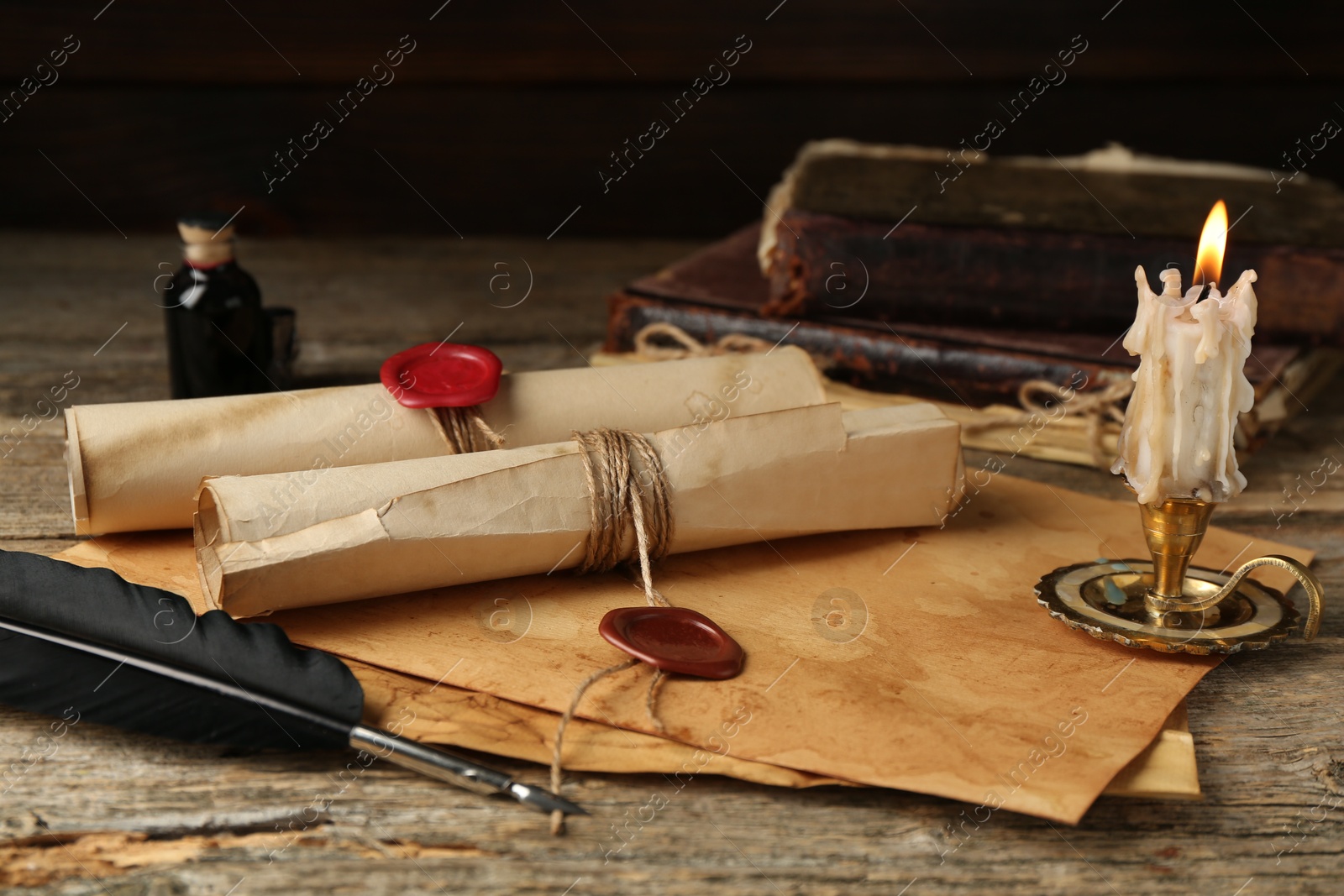 Old paper scrolls and burning candle on wooden table, closeup Photo of Old paper scrolls and burning candle on wooden table, closeup