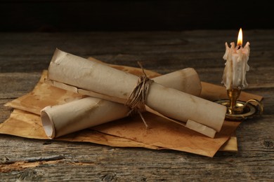 Photo of Old paper scrolls and burning candle on wooden table, closeup