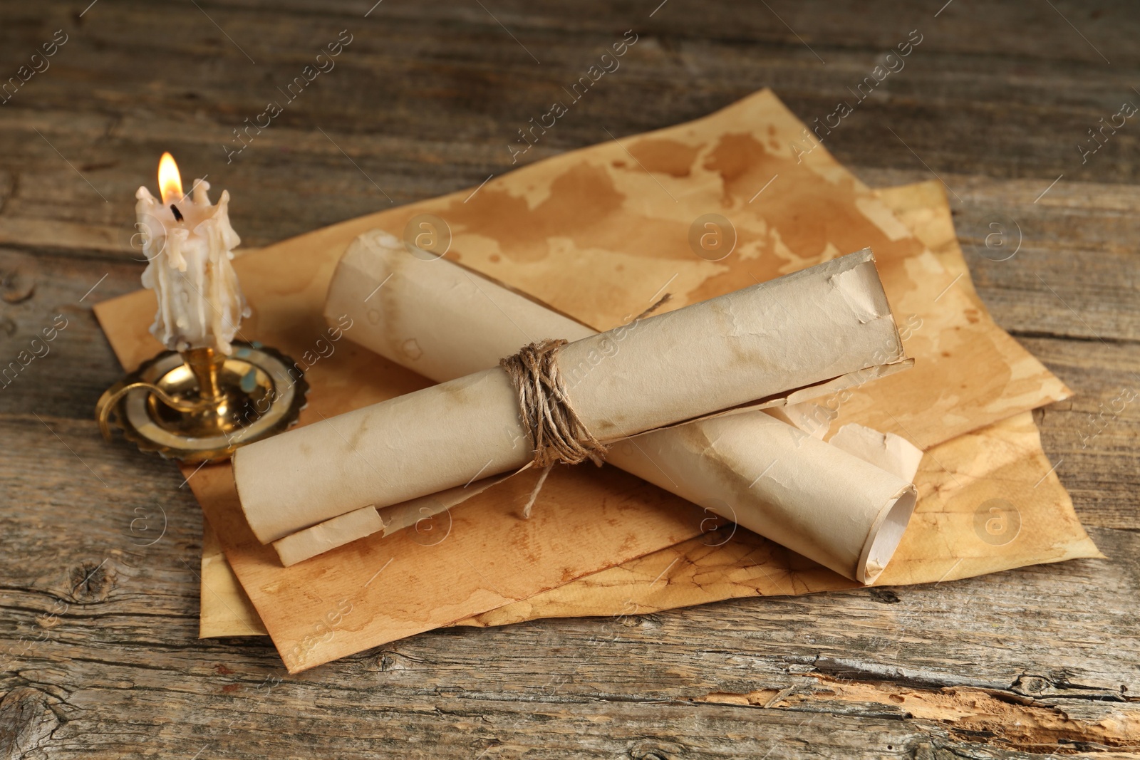 Old paper scrolls and burning candle on wooden table, closeup Photo of Old paper scrolls and burning candle on wooden table, closeup