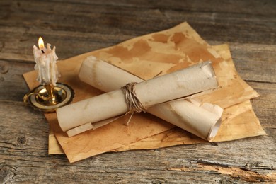 Photo of Old paper scrolls and burning candle on wooden table, closeup