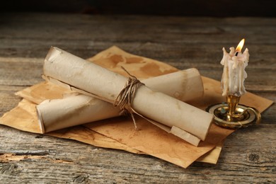Photo of Old paper scrolls and burning candle on wooden table, closeup