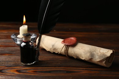 Photo of Old rolled scroll, burning candle, feather and inkwell on wooden table, closeup