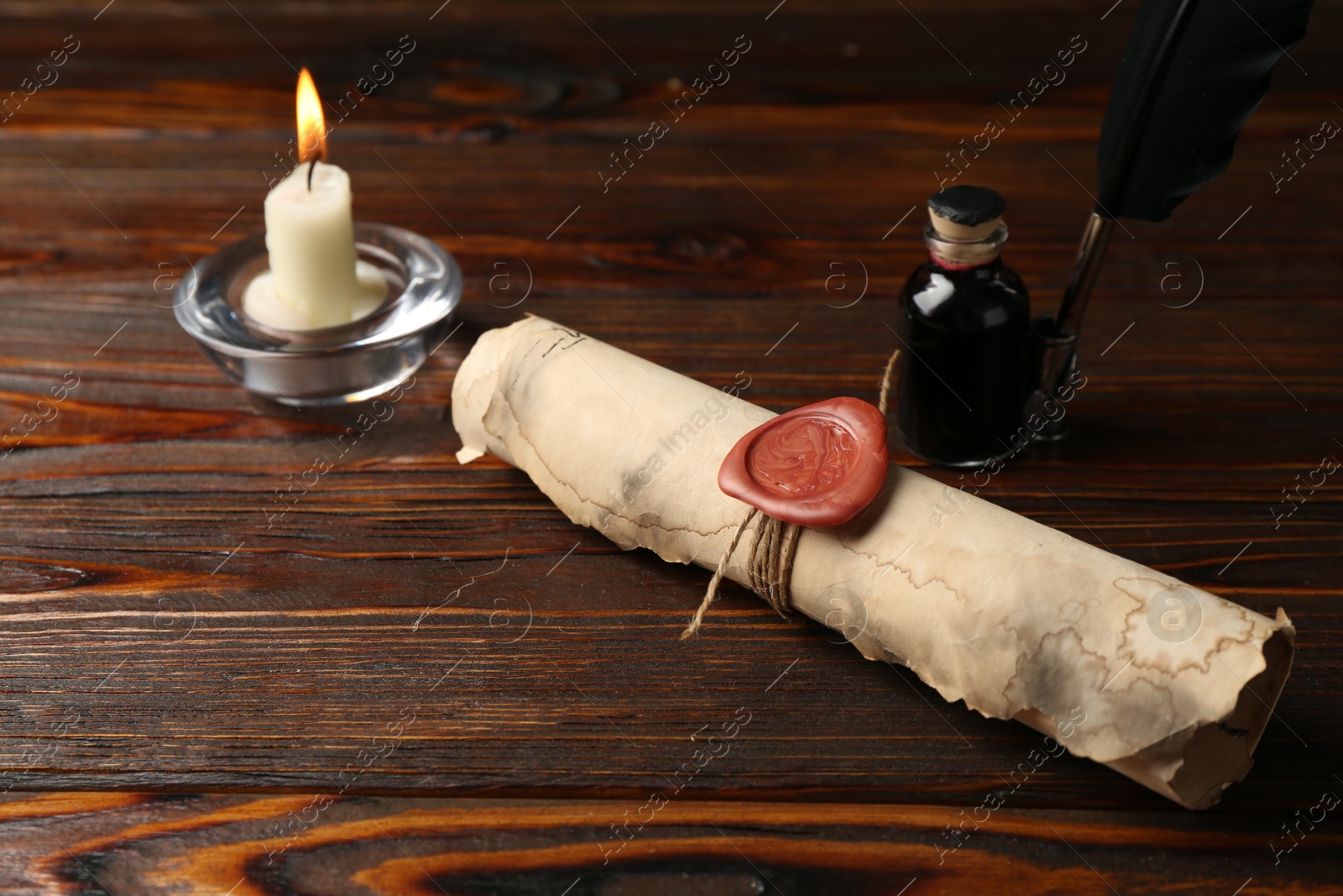 Old rolled scroll, burning candle, feather and inkwell on wooden table, closeup Photo of Old rolled scroll, burning candle, feather and inkwell on wooden table, closeup