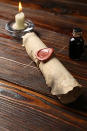 Photo of Old rolled scroll, burning candle and inkwell on wooden table, closeup