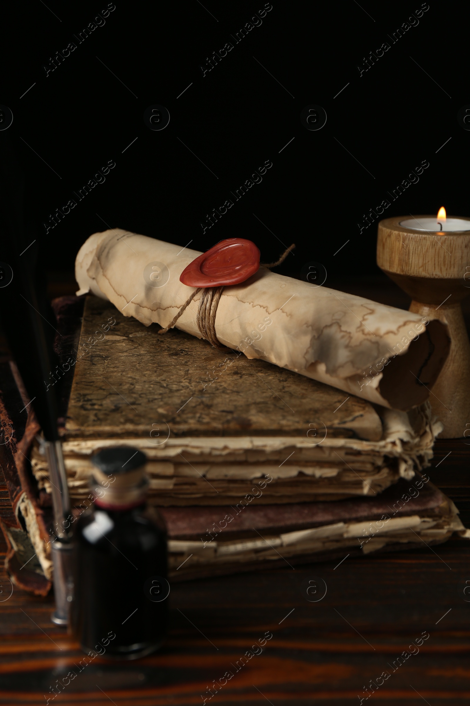 Old rolled scroll, burning candle, feather, inkwell and books on wooden table, closeup Photo of Old rolled scroll, burning candle, feather, inkwell and books on wooden table, closeup