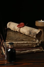 Photo of Old rolled scroll, burning candle, feather, inkwell and books on wooden table, closeup