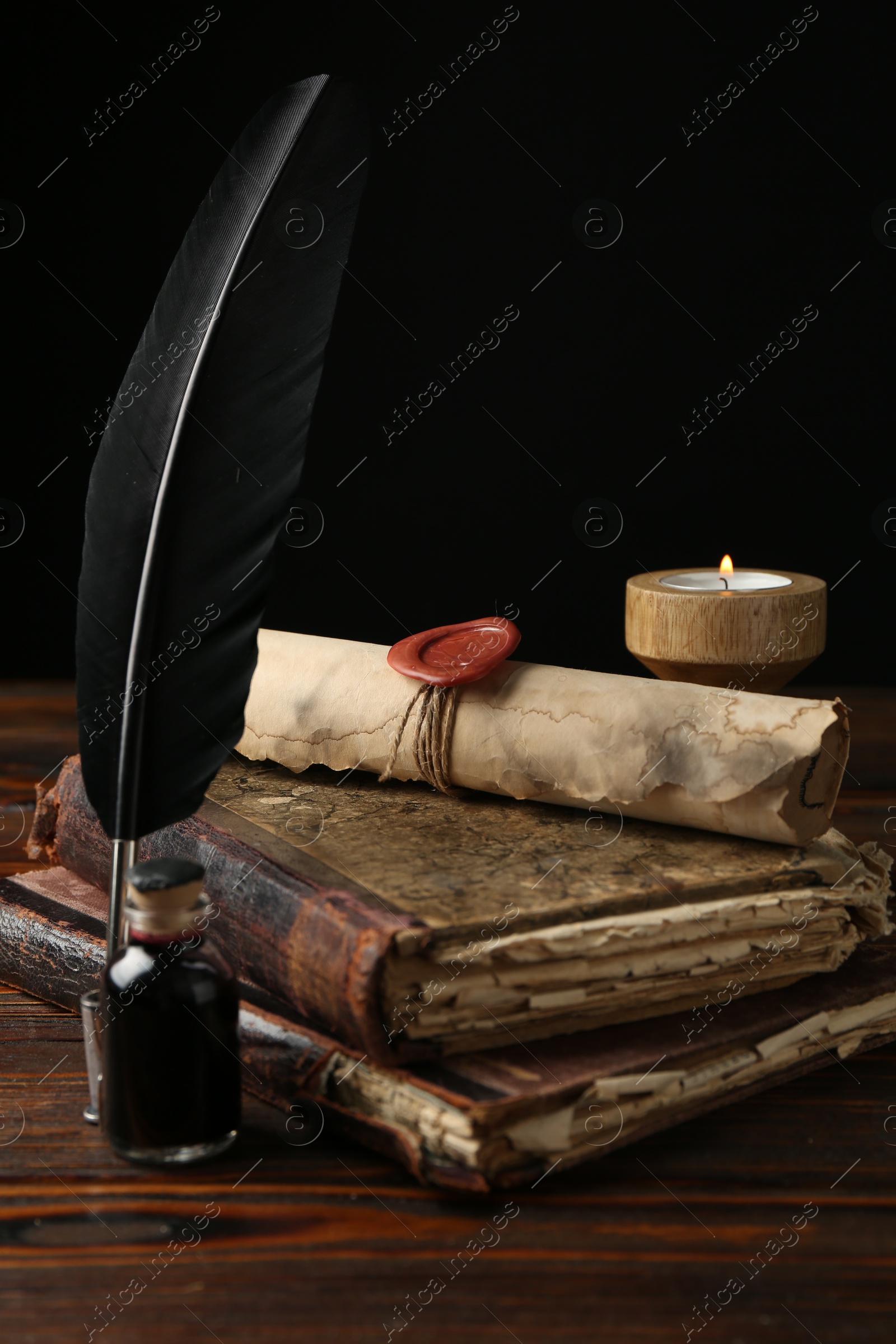 Old rolled scroll, burning candle, feather, inkwell and books on wooden table, closeup Photo of Old rolled scroll, burning candle, feather, inkwell and books on wooden table, closeup