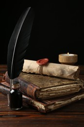 Photo of Old rolled scroll, burning candle, feather, inkwell and books on wooden table, closeup