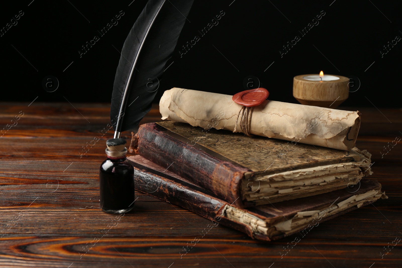 Old rolled scroll, burning candle, feather, inkwell and books on wooden table, closeup Photo of Old rolled scroll, burning candle, feather, inkwell and books on wooden table, closeup