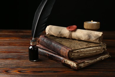 Photo of Old rolled scroll, burning candle, feather, inkwell and books on wooden table, closeup