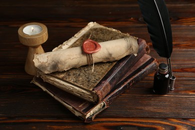 Photo of Old rolled scroll, burning candle, feather, inkwell and books on wooden table, closeup