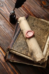 Photo of Old rolled scroll, feather, inkwell and books on wooden table, closeup