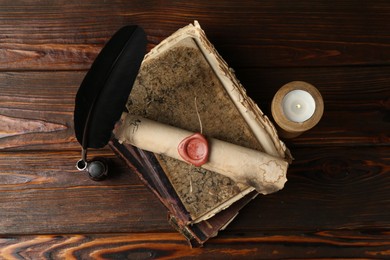 Photo of Old rolled scroll, burning candle, feather, inkwell and books on wooden table, flat lay