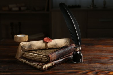 Photo of Old rolled scroll, burning candle, feather, inkwell and books on wooden table