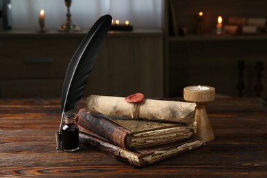 Photo of Old rolled scroll, burning candle, feather, inkwell and books on wooden table