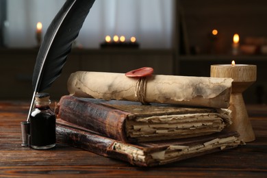 Photo of Old rolled scroll, burning candle, feather, inkwell and books on wooden table, closeup