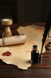 Photo of Paper scrolls, burning candle, feather, inkwell and books on wooden table, closeup