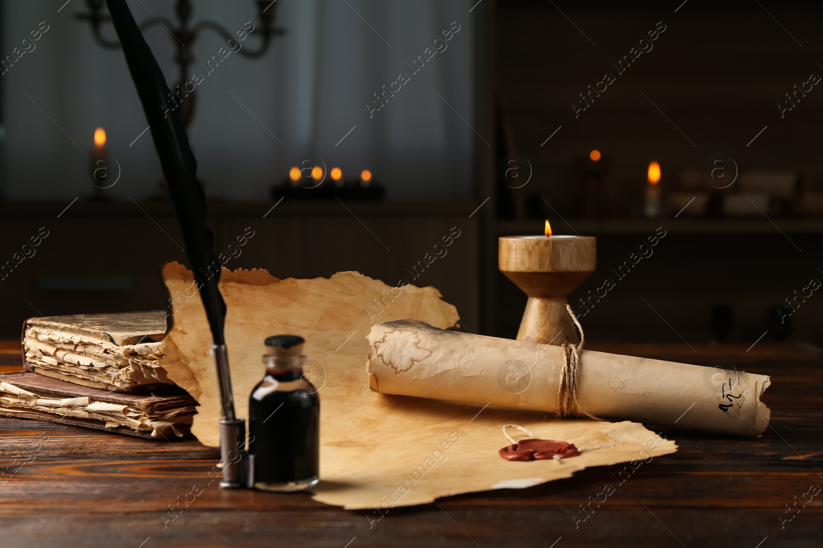 Paper scrolls, burning candle, feather, inkwell and books on wooden table, closeup Photo of Paper scrolls, burning candle, feather, inkwell and books on wooden table, closeup
