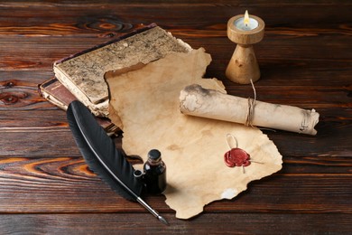 Photo of Paper scrolls, burning candle, feather, inkwell and books on wooden table