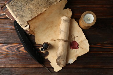 Photo of Paper scrolls, burning candle, feather, inkwell and books on wooden table, flat lay