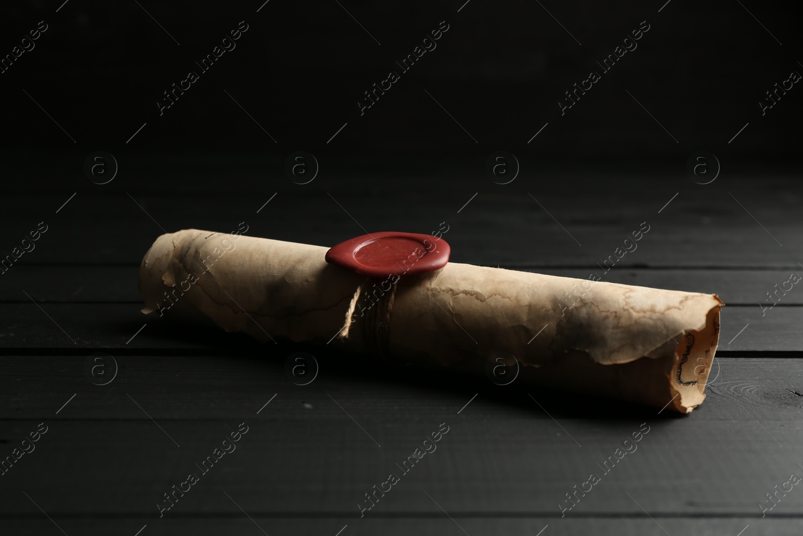 One old rolled scroll with wax seal on black wooden table, closeup Photo of One old rolled scroll with wax seal on black wooden table, closeup
